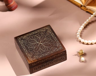 May include: A small, square wooden box with a decorative floral design inlaid in gold. The box is closed and has a dark brown finish.