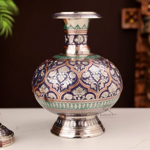 Puede incluir: Un jarrón de plata con intrincados diseños florales en azul, verde y naranja. El jarrón tiene un cuerpo redondo y un cuello estrecho.