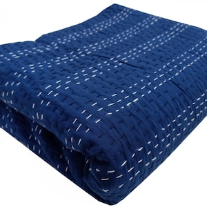 Peut inclure: Couverture pliée bleu indigo avec des lignes cousues blanches. La couverture a une surface texturée et un motif géométrique créé par les coutures. Les bords pliés montrent l'épaisseur du tissu.