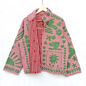 May include: A long-sleeved jacket featuring a pink and white geometric pattern with green embroidered motifs including a sun, a bird, a teacup, and stars. The inner placket displays a red and white vertical stripe pattern with red buttons.
