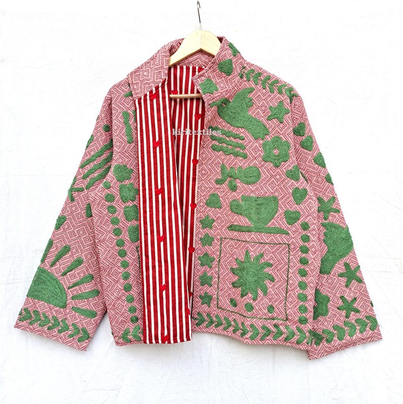May include: A long-sleeved jacket featuring a pink and white geometric pattern with green embroidered motifs including a sun, a bird, a teacup, and stars. The inner placket displays a red and white vertical stripe pattern with red buttons.