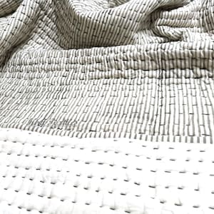 Può includere: Una trapunta di cotone a righe bianche e grigie con un design semplice cucito a mano. La trapunta è realizzata in tessuto morbido e traspirante ed è perfetta per aggiungere un tocco di calore e stile a qualsiasi camera da letto.