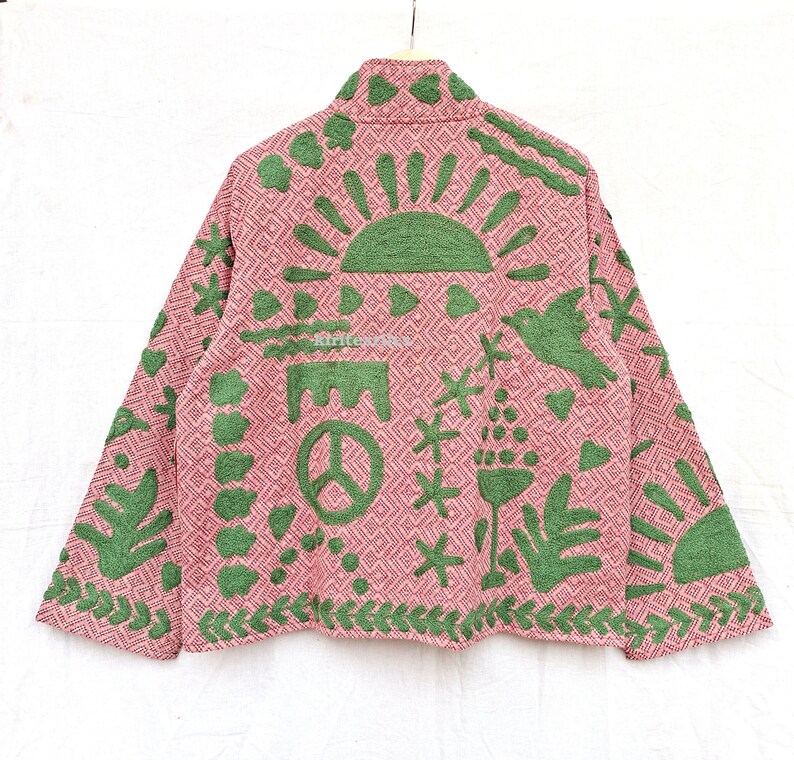 May include: A long-sleeved jacket in a dusty pink hue featuring a repeating geometric diamond pattern. The garment is adorned with raised green textured appliques depicting a sun, a peace sign, a bird, hearts, and various botanical motifs.