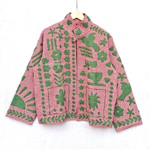 May include: A long-sleeved jacket in a dusty pink hue featuring a geometric diamond pattern and raised green embroidery. The design includes motifs of flowers, birds, stars, and a sun. The text "kidtextiles" is visible on the front panel.