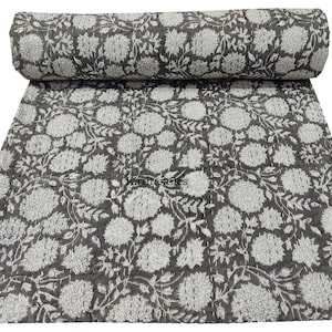 Puede incluir: Un edredón floral gris enrollado, con un patrón repetido de flores y hojas blancas. El edredón está hecho de una tela suave y es adecuado para una cama o un sofá. El texto "Kiritextiles" es visible.