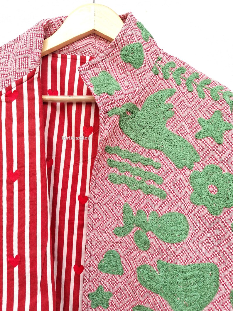May include: A jacket featuring a red and white geometric pattern on the exterior with green textured appliqu&eacute;s of a bird, flower, and stars. The interior lining is red and white striped fabric with small red heart accents and the text kiritextiles.