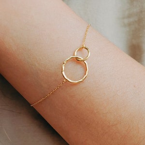 May include: A gold chain bracelet with two connected circles. The larger circle is textured and the smaller circle is smooth.