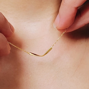 Puede incluir: Un delicado collar de cadena de oro con un colgante simple y curvo.