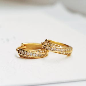 以下が含まれることがあります： 金色のフープイヤリングのペア。各フープの縁には、透明なキュービックジルコニアの石が並んでいます。