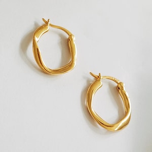 May include: A pair of gold-toned hoop earrings with a slightly irregular, organic shape.