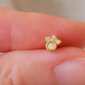 May include: A gold-toned earring featuring a small opal gemstone and a cluster of clear cubic zirconia stones.