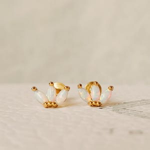 Op de afbeelding: Een paar gouden oorbellen met witte opaalstenen. De oorbellen hebben de vorm van een kroon met drie stenen aan elke kant.