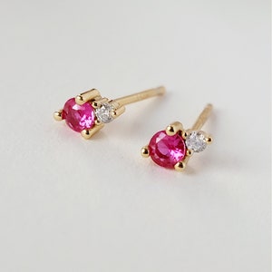 Puede incluir: Un par de pendientes de oro con una piedra preciosa rosa y una piedra blanca más pequeña.