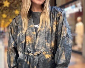 May include: A black leather jacket with gold accents. The jacket has a relaxed fit and a collarless design.