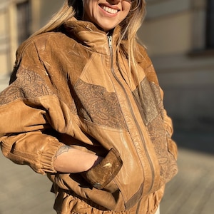 Peut inclure: Une veste en cuir marron avec une fermeture éclair et un design patchwork. La veste a un col montant et un ourlet côtelé.