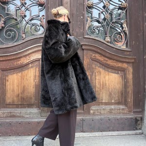May include: A long-sleeved, dark charcoal faux fur coat with a high collar, paired with dark brown wide-leg trousers and black leather ankle boots with a pointed toe and a mid-height heel, worn by an individual with blonde hair in a bun.