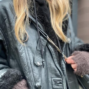 May include: A black leather jacket with a fur-lined hood and a zipper closure. The jacket has a chain detail and a button closure at the waist.