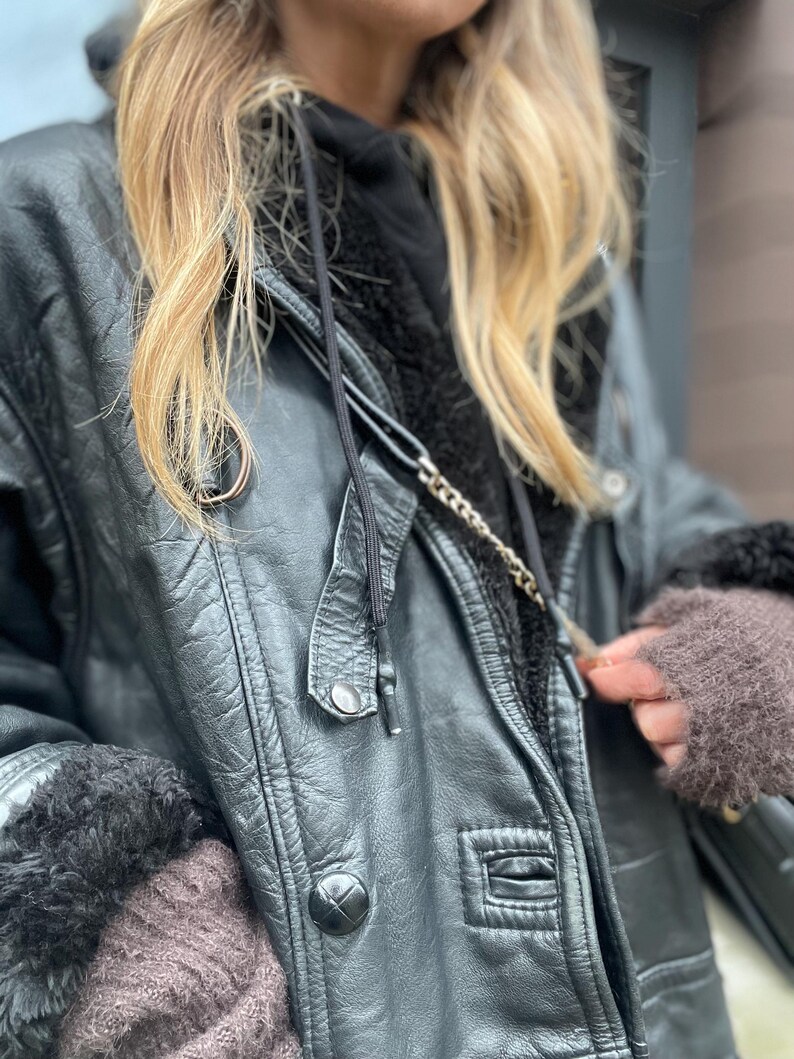 May include: A black leather jacket with a fur-lined hood and a zipper closure. The jacket has a chain detail and a button closure at the waist.