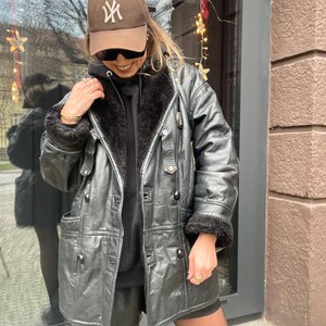 May include: A black leather jacket with a fur collar and a brown baseball cap with the New York Yankees logo.