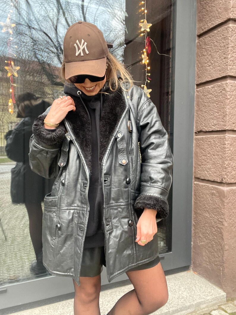 May include: A black leather jacket with a fur collar and a brown baseball cap with the New York Yankees logo.