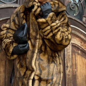 Può includere: Un cappotto in pelliccia sintetica a maniche lunghe con motivo marrone e marrone chiaro e un ampio colletto, abbinato a guanti in pelle nera e una pochette in pelle nera. Il cappotto presenta un motivo geometrico a griglia marrone scuro.