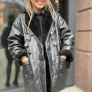 May include: A black leather jacket with a fur collar and pockets. The jacket has a button closure and a belt.