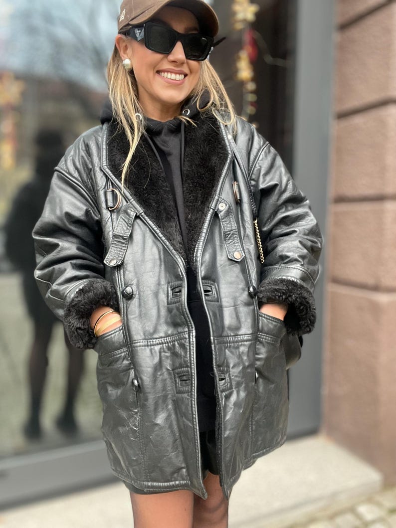 May include: A black leather jacket with a fur collar and pockets. The jacket has a button closure and a belt.