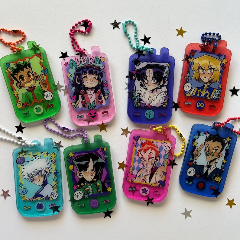 May include: A collection of eight translucent acrylic keychains shaped like vintage handheld game consoles, each featuring a unique anime-style character illustration, colorful ball chains, and small decorative star-shaped cutouts.