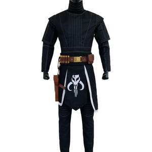 May include: A black costume set featuring a high-neck long-sleeve top with vertical stitching, matching trousers, and a brown utility belt with gold accents. A black apron-style piece displays a white skull emblem, accompanied by a brown holster.