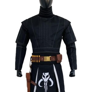 May include: A black long-sleeved tunic with vertical stitching, a high collar, and shoulder padding. A brown leather belt features gold-colored ammunition loops, a metallic buckle, and a holster. A black apron displays a white skull emblem.