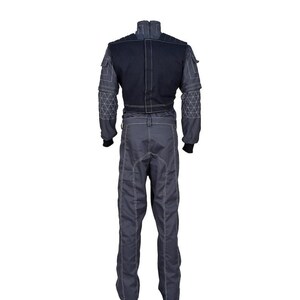 May include: A dark gray and black jumpsuit featuring a high collar, long sleeves with geometric white stitching patterns, and a solid black upper back panel. The garment includes utility-style pockets on the shoulders and white contrast stitching.
