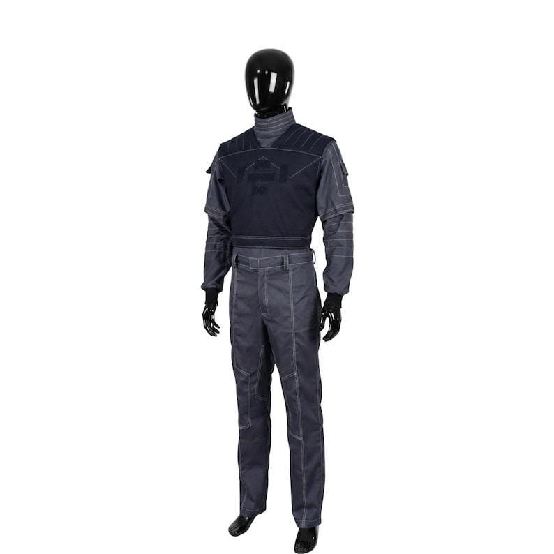 May include: A dark gray long-sleeved jumpsuit featuring a black chest overlay with ribbed shoulder detailing. The garment includes a high mock neck collar, fitted cuffs, and prominent white topstitching throughout the torso, sleeves, and trousers.