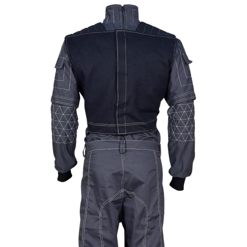 May include: A dark gray and black jumpsuit featuring a high collar, long sleeves with white geometric stitching patterns, and a solid black upper back panel. The garment includes a belt, utility pockets on the shoulders, and white contrast stitching.