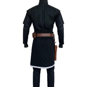 May include: A black long-sleeved tunic with a high collar and white stitching details, paired with a brown leather belt featuring a pouch and holster. The lower section of the tunic has a quilted texture and a white hem, worn over black trousers.