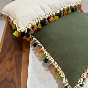 May include: Two decorative throw pillows with a white and green fabric and a fringe trim with black, orange, and green tassels.
