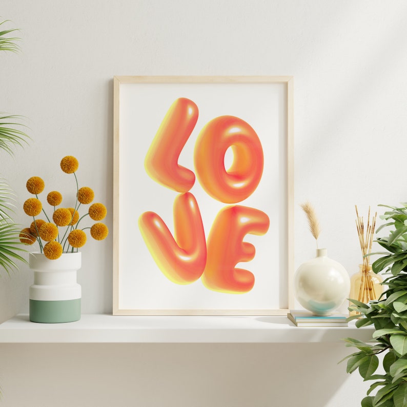 Puede incluir: Una impresi&oacute;n enmarcada con la palabra "LOVE" en letras grandes, 3D, naranja y amarillo. Las letras est&aacute;n estilizadas para parecer globos.