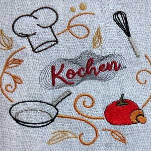 May include: Embroidered kitchen towel featuring a chef's hat, whisk, frying pan, and tomato. The word "Kochen" is embroidered in red. The design is surrounded by decorative swirls and leaves, in brown and gold.
