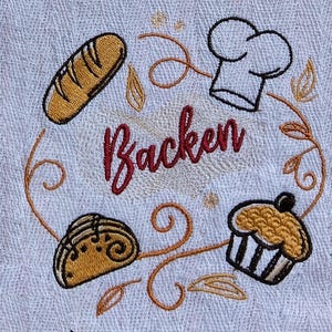 Könnte beinhalten: Weißes, besticktes Küchentuch mit Backmotiv. Es zeigt ein Brot, eine Kochmütze, einen Muffin und ein Gebäck, alles in einem kreisförmigen Design um das Wort "Backen" in burgunderfarbener Schrift. Das Design ist in Braun- und Schwarztönen gehalten.