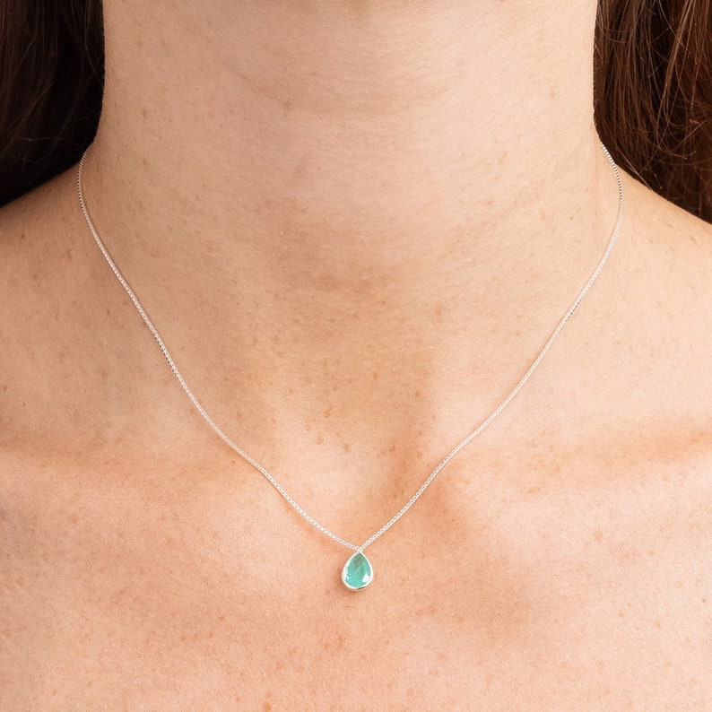May include: A silver chain necklace with a teardrop-shaped light blue gemstone pendant.