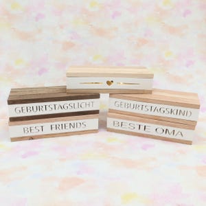 Può includere: Quattro blocchi di legno con lettere bianche. I blocchi recitano "Geburtstagslicht", "Best Friends", "Geburtstagskind" e "Beste Oma".