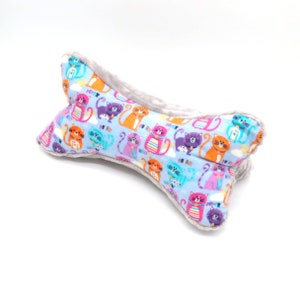 May include: A bone-shaped pillow with a light blue fabric featuring a repeating pattern of colorful cartoon cats. The pillow is trimmed with a soft gray fabric.