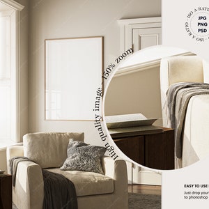 May include: A beige armchair with a gray throw blanket and a gray pillow in a living room with a large window and a framed picture on the wall.