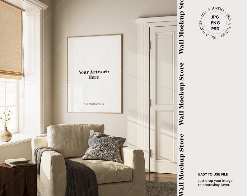 May include: A beige armchair with a throw blanket and pillows sits in a living room with a framed mockup of artwork on the wall. The room has a large window with blinds and a door.
