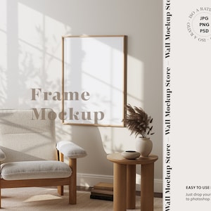 May include: A vertical frame mockup with a wooden frame hangs on a neutral wall. A light-colored armchair and a small wooden side table with a vase and decorative items are in front of the wall. The text "Frame Mockup" is visible.