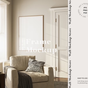 May include: A beige armchair with a gray throw blanket and a pillow sits in a room with a large window and a framed picture on the wall. The room has a light brown wooden floor.