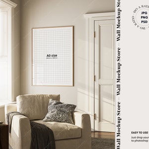 May include: A beige armchair with a gray throw blanket and a gray pillow sits in a room with a large window and a framed print on the wall. The print is labeled "A0 size".