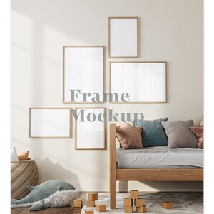 Puede incluir: Un interior de sala de estar con una cama de día de madera y cinco marcos de fotos vacíos en la pared. Los marcos son de diferentes tamaños y están dispuestos en un patrón escalonado. La cama de día tiene un colchón gris claro y está cubierta con almohadas en varios tonos de marrón y azul. La pared está pintada de color beige claro.