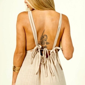 May include: A beige linen dress with a low back and a tie detail. The dress has a relaxed fit and a flowy silhouette.