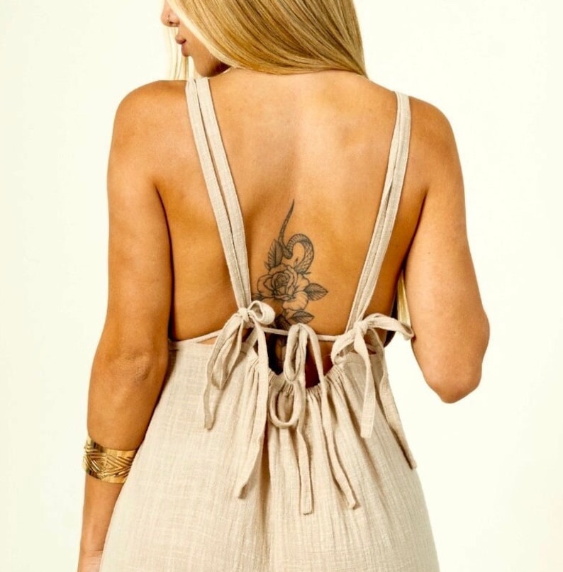 May include: A beige linen dress with a low back and a tie detail. The dress has a relaxed fit and a flowy silhouette.