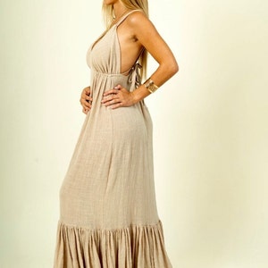 May include: A long, flowy, beige maxi dress with a V-neckline and a tiered skirt. The dress has a relaxed fit and is made of a lightweight fabric.